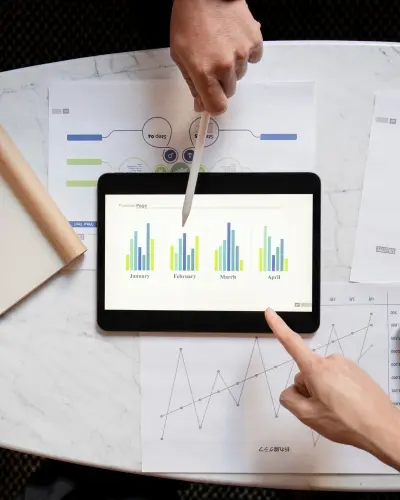 Analyst pointing at a bar chart on a tablet beside printed performance reports