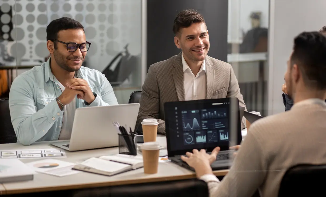 IT consultants reviewing a dashboard on a tablet with a client across a meeting table